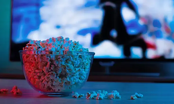 Popcorn in a glass plate on the background of the TV. Color bright lighting, blue and red. Background