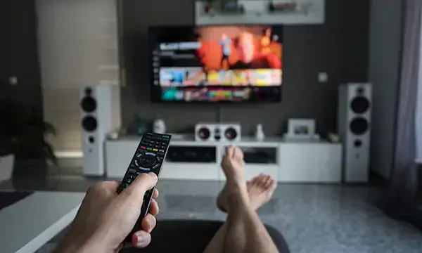 A young man is browsing through television channels with a remote control.