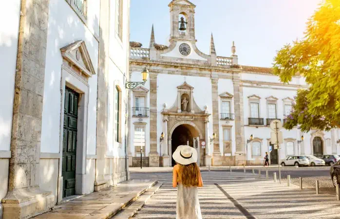 Young woman tourist standing on the city gate background in Faro town on the south of Portugal