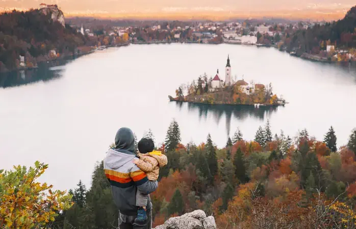 Father and his son looking sunset with amazing view on Bled Lake. Autumn or Winter in Slovenia, Europe. Top view on Island with Catholic Church in Bled Lake with Castle and Mountains in Background.