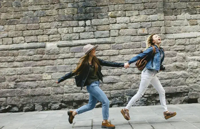 Spain, Barcelona, two young women running hand in hand in the city