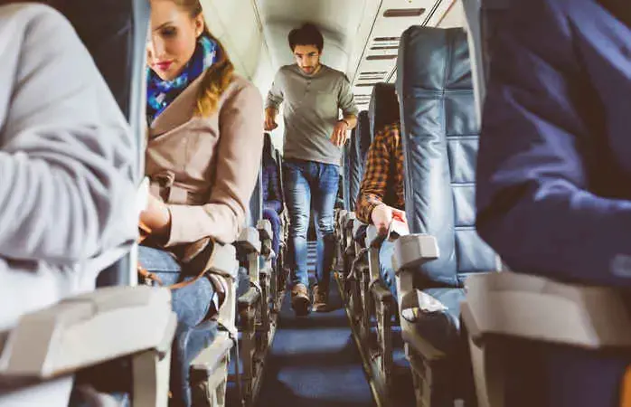Passengers on seat during flight with man walking in aisle. Interior of airplane with people sitting on seats. People traveling by plane.